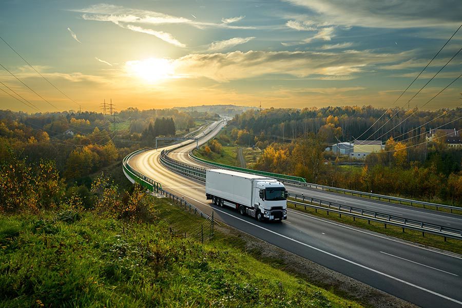 Business Insurance - White Truck Traveling on a Long Highway at Dusk, Landscape Full of Trees Turning Colors for Fall